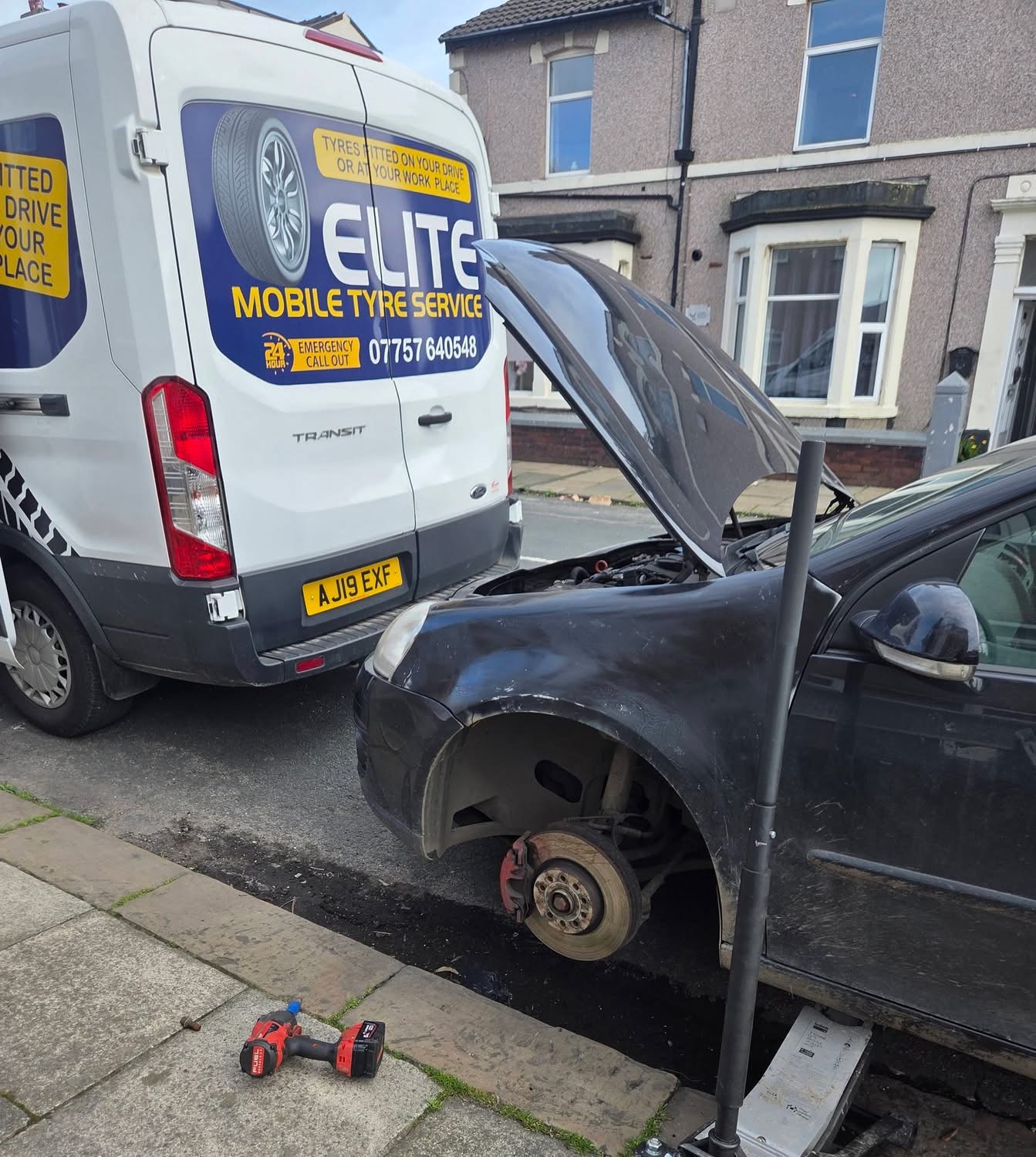 Emergency mobile tyre replacement in Leeds — Elite technician using a trolley jack to remove a kerbed alloy wheel from a black hatchback