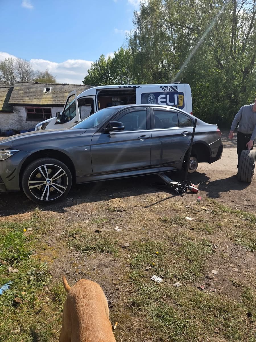 Performance tyre fitting for a BMW 3 Series M-Sport — Elite technician wheeling a new tyre to a jacked-up BMW at a Yorkshire yard