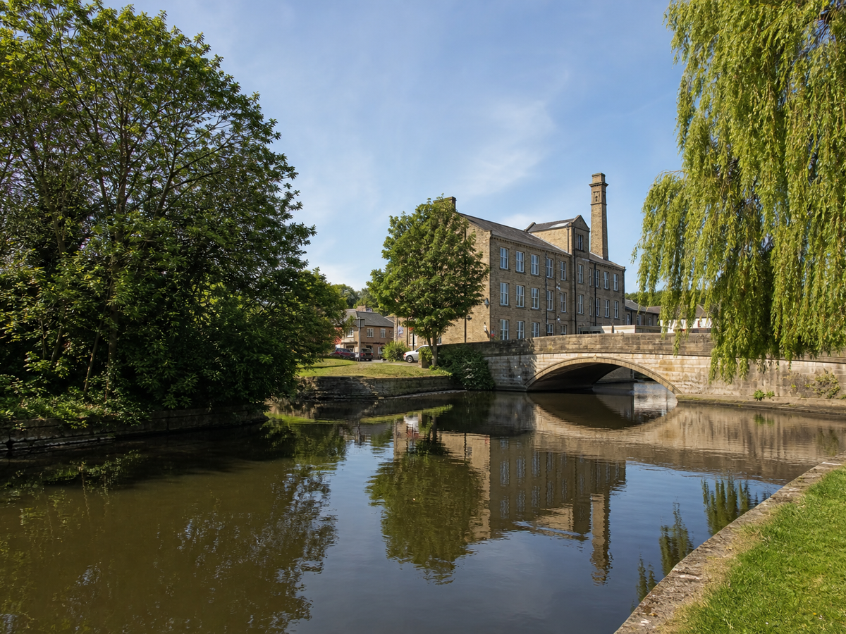 A historic stone building and arched bridge are reflected in a calm river.